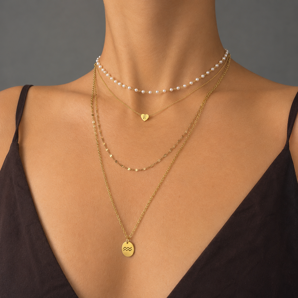Gold-tone stainless steel maximalist layered necklace stack with pearl choker, heart initial pendant, and zodiac charm
